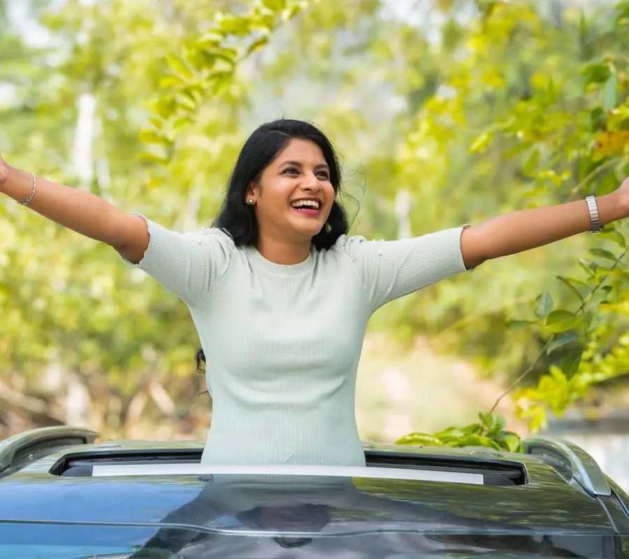 A woman with arms open, smiling and breathing in fresh air through a car sunroof